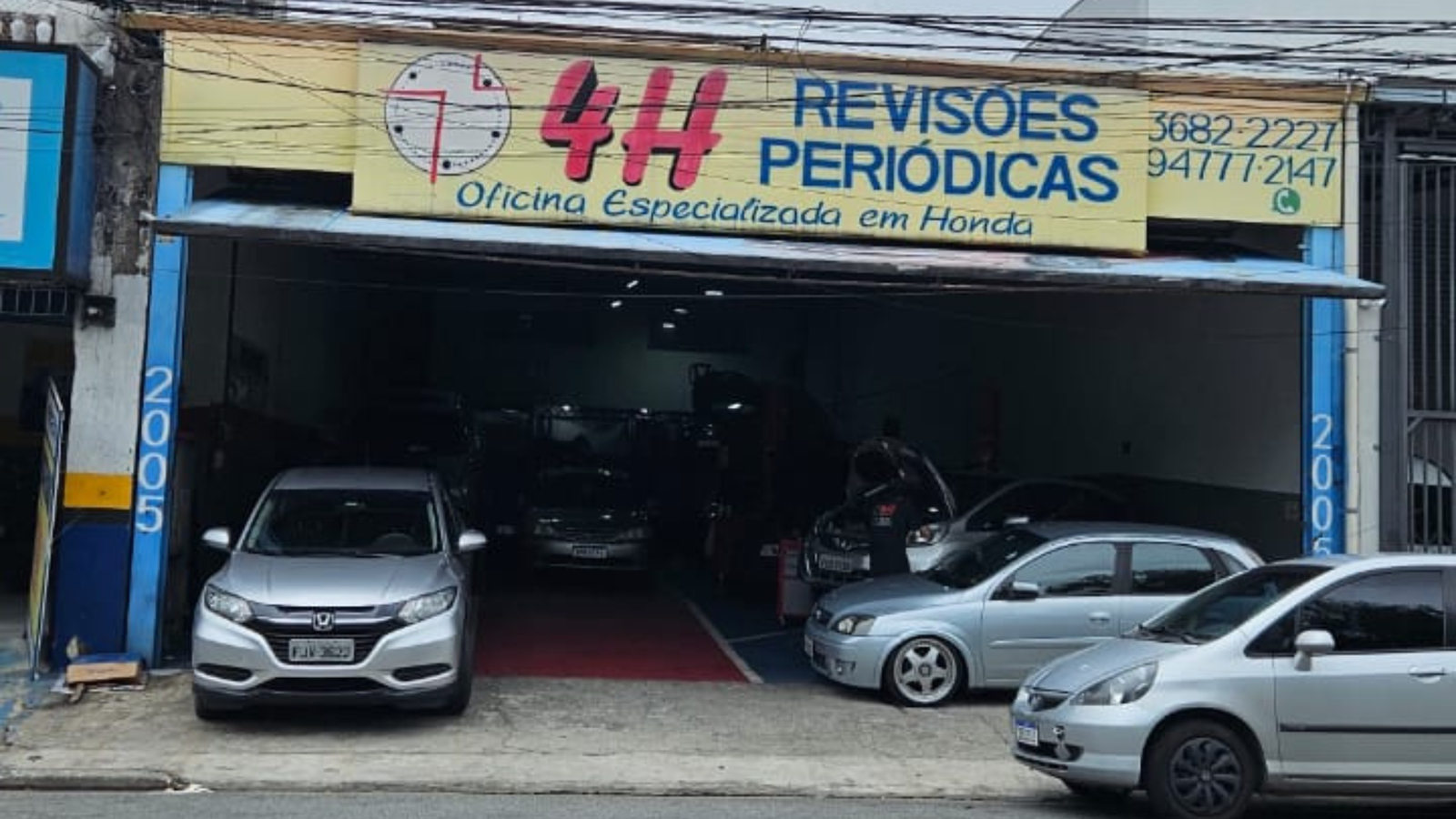 Fachada da Oficina 4H em Osasco mostrando o letreiro amarelo de Revisões Periódicas e carros Honda em elevadores automotivos.